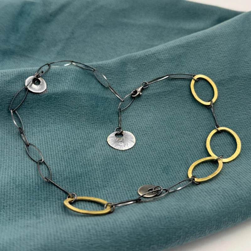 Krótki naszyjnik z oksydowanego srebra z mosiężnymi owalami na turkusowej tkaninie